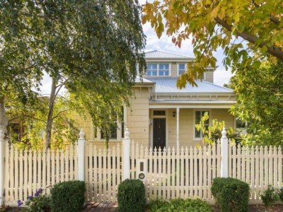 a white house with a fence and trees in the front