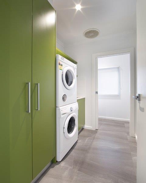 Compact laundry with green cabinetry and stacked washer and dryer
