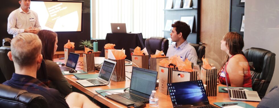 a group of people sitting around a table with laptops