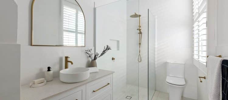 White bathroom with an arched mirror and glass shower screen